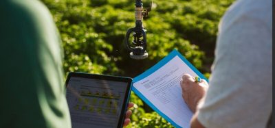 Two professionals reviewing documents in a field, discussing regenerative agriculture practices and farmer support programs.