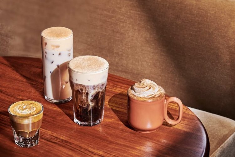Two Starbucks autumn drinks, a Pumpkin Spice Latte and a Pecan Oatmilk Cortado, sitting side by side on a wooden coffee table.