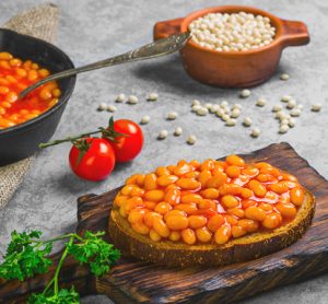 Braised beans in tomato sauce in cast iron pan. Vegetarian sandwiches with bean. Open sandwiches with bread, stewed white beans. Raw white beans, pieces of rye bread for sandwiches. Grey background.