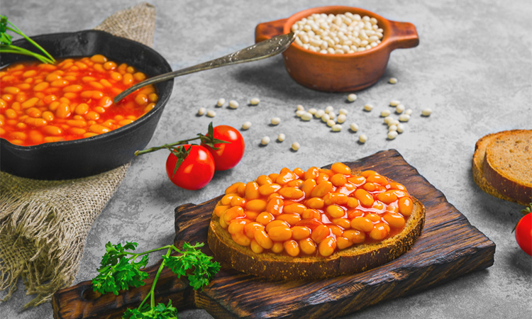 Braised beans in tomato sauce in cast iron pan. Vegetarian sandwiches with bean. Open sandwiches with bread, stewed white beans. Raw white beans, pieces of rye bread for sandwiches. Grey background.