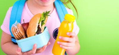 Young schoolgirl with lunch box on a green background. Little girl with a school backpack and a set of food for a snack. Free space for text