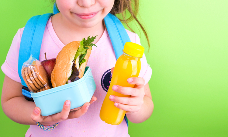 Young schoolgirl with lunch box on a green background. Little girl with a school backpack and a set of food for a snack. Free space for text