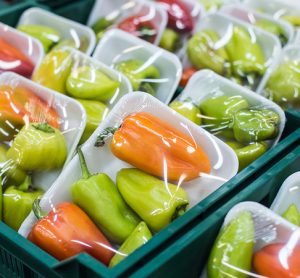 Peppers in a box covered in plastic food packaging on a shelf in a supermarket