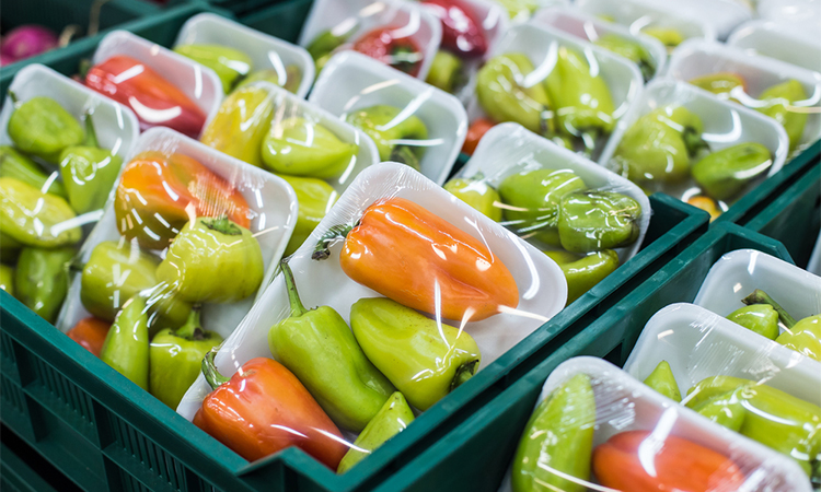 Peppers in a box covered in plastic food packaging on a shelf in a supermarket