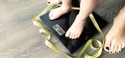 The feet of a child standing on a weighing scale with the LCD depicting the word "help". A parent stands behind.