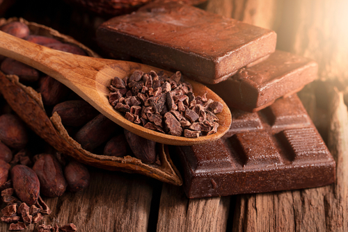 Cocoa beans and a cocoa pod on a wooden surface, representing the source of chocolate and the challenges in sustainable cocoa farming.